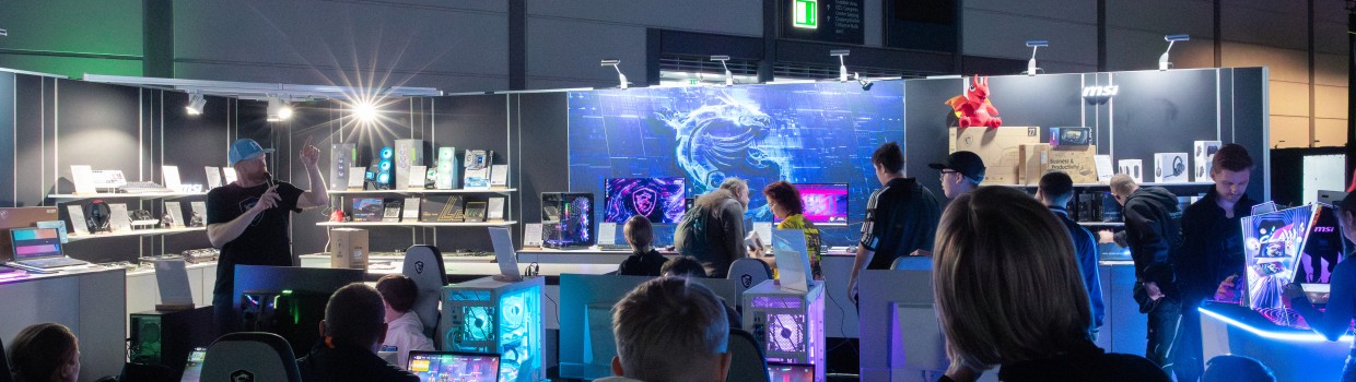 Besucher schauen sich einen bunten Stand mit Gamign Hardware an.